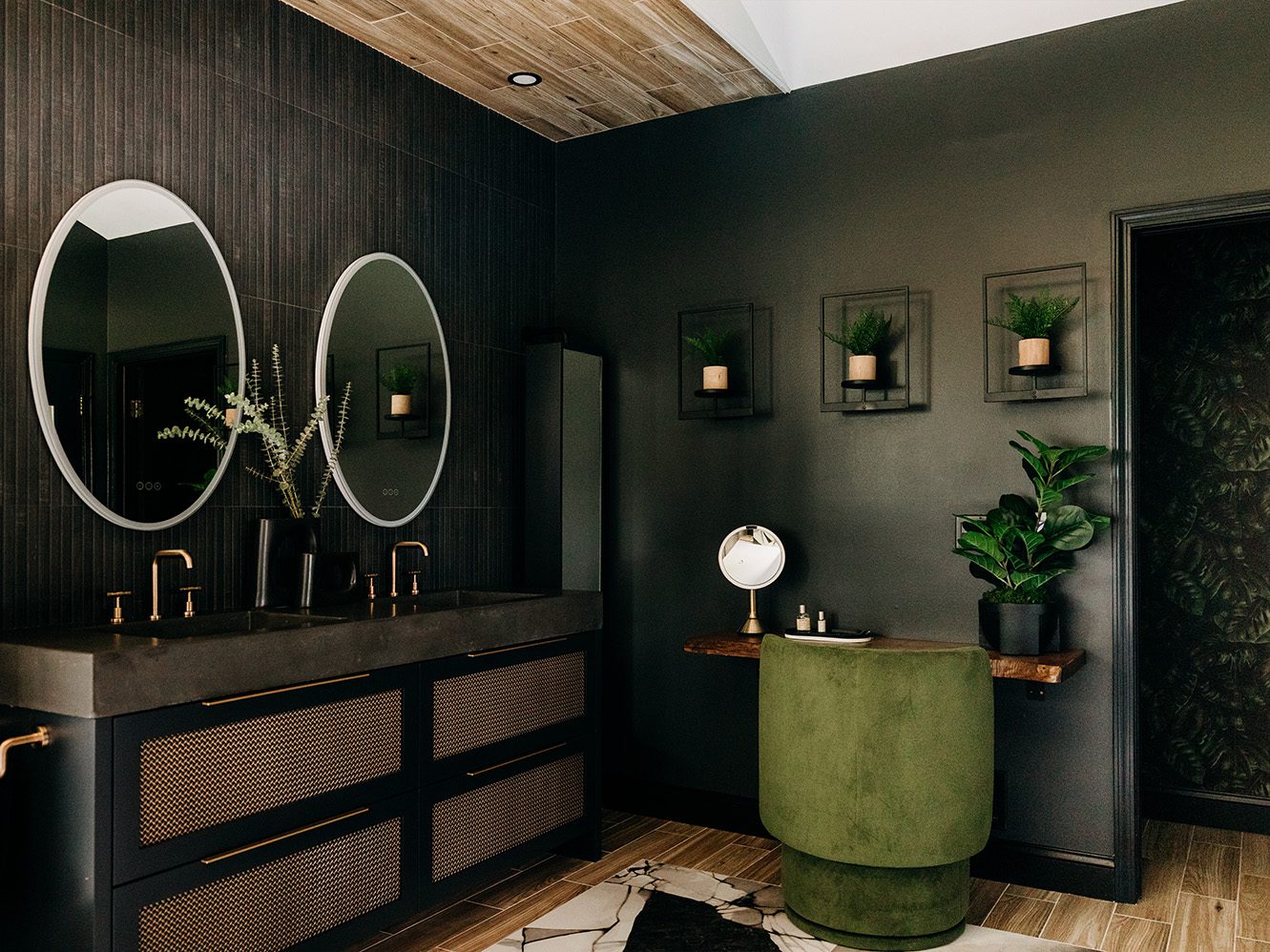 Primary bathroom after renovation, with oval mirrors, a textured dark wall, and a cane-front double vanity.