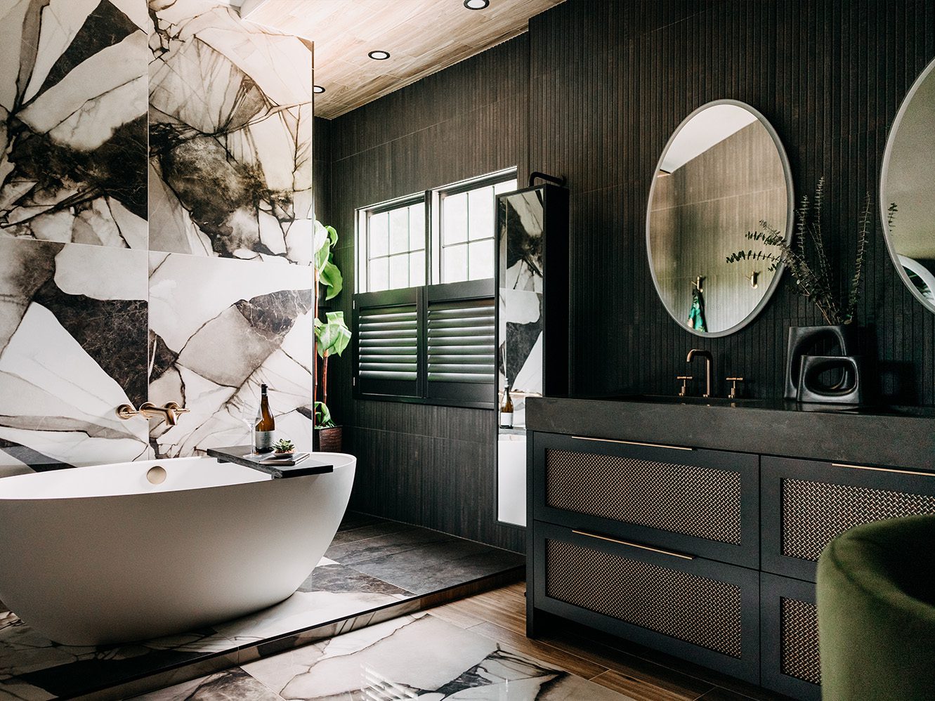 Primary bathroom after renovation, with a freestanding tub, dramatic stone wall, and warm wood-look ceiling.
