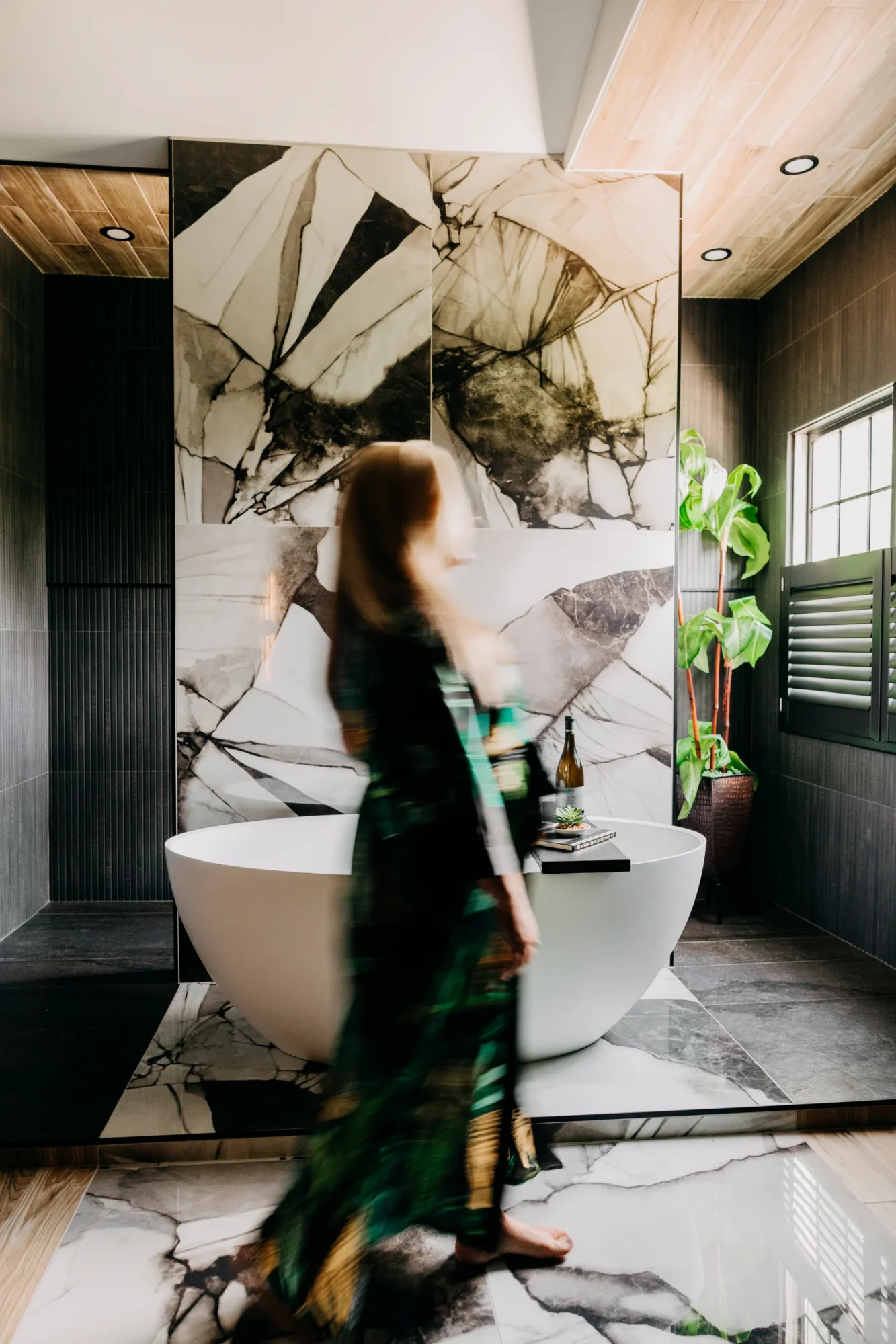 Homeowner beside the freestanding tub beneath the wood ceiling.