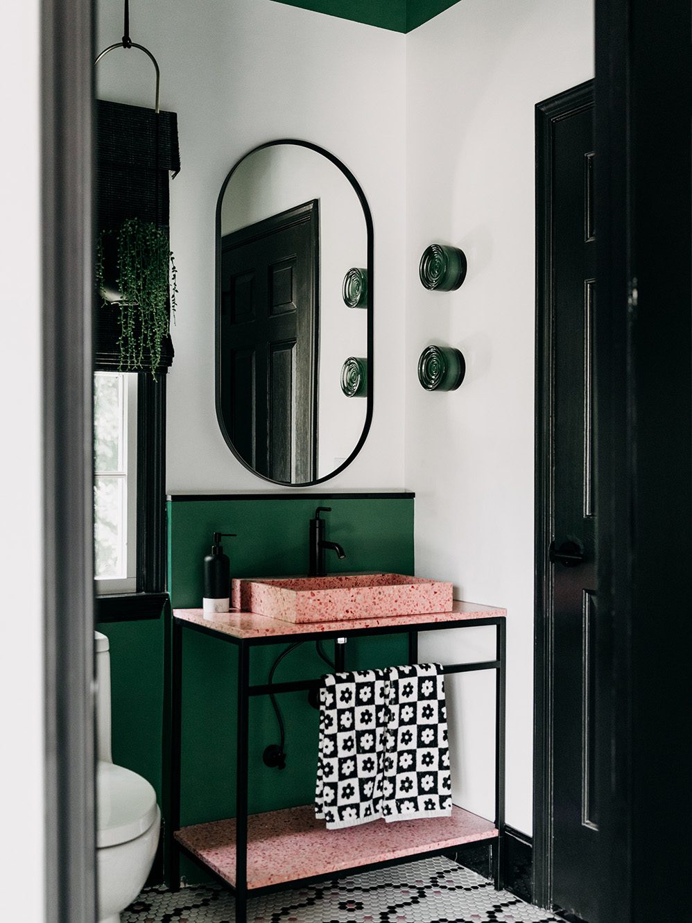 Secondary bathroom vanity after renovation, with a pink terrazzo console sink, oval mirror, and green tile.