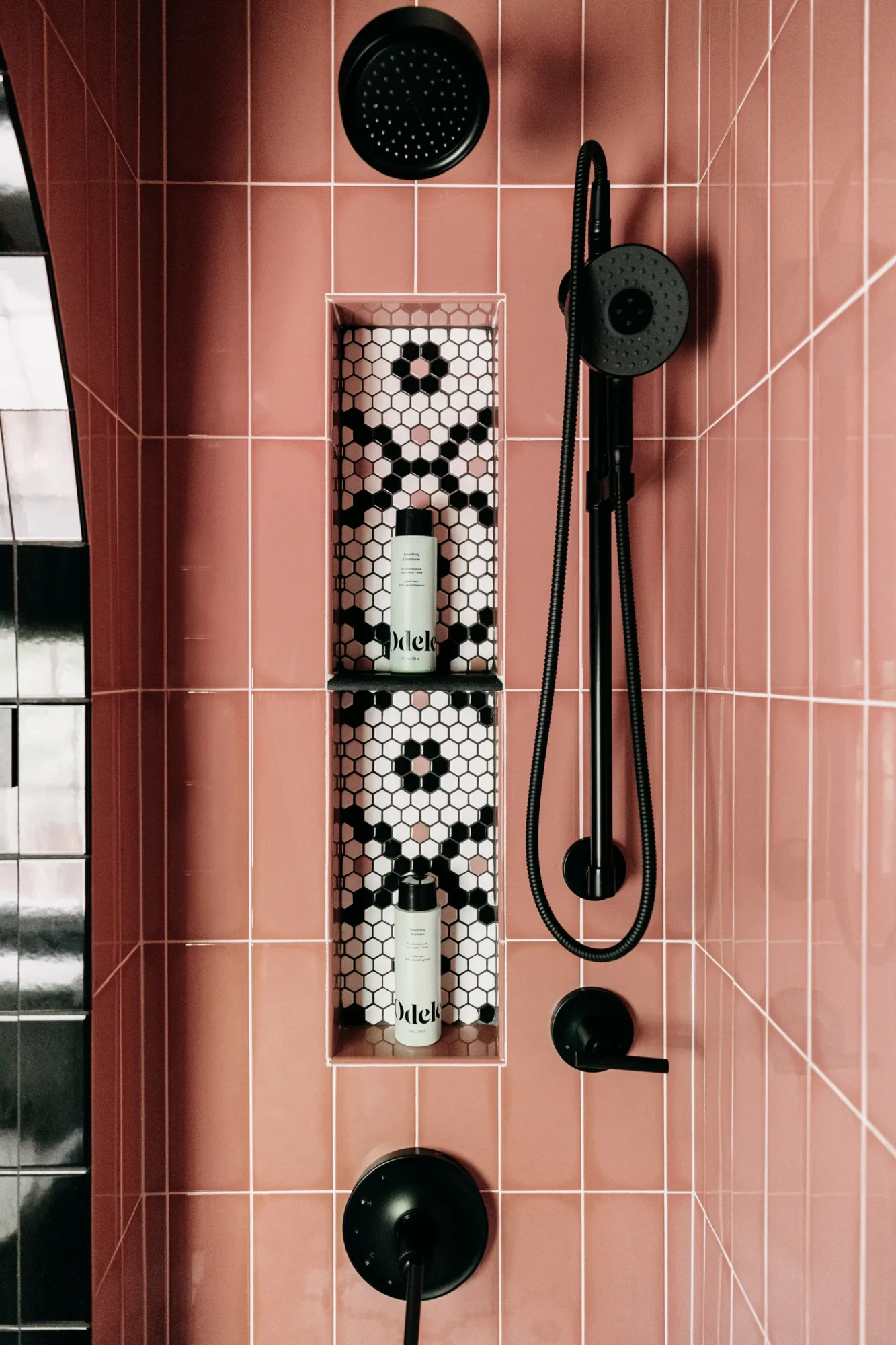 Black shower fixtures and patterned recessed niche on the pink tile wall.