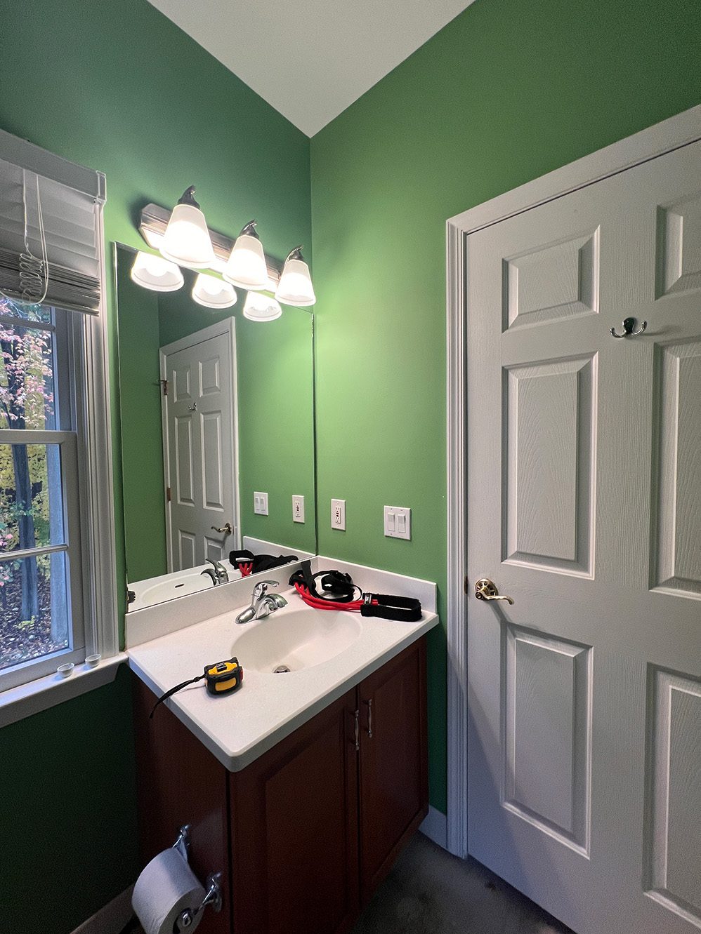 Secondary bathroom vanity before renovation, with green walls, a large mirror, and a traditional white sink.